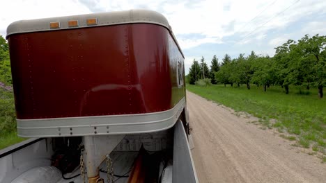 Pulling-horse-trailer-with-pickup-truck-on-gravel-road,-back-POV