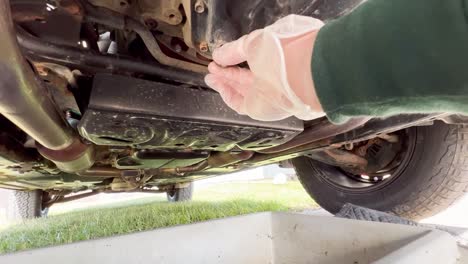 Unplugging-an-oil-pan-from-the-bottom-of-an-SUV-wearing-a-rubber-glove