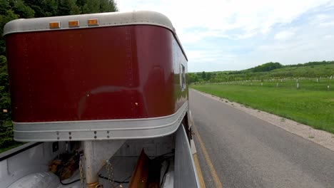 Pickup-truck-pulls-horse-trailer-in-countryside-road-fast,-back-POV-view