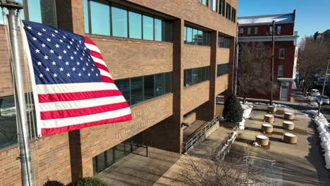 Luftaufnahme-Der-Amerikanischen-Flagge,-Die-An-Einem-Verschneiten-Tag-Vor-Dem-Bundesgebäude-Und-Dem-Gerichtsgebäude-Der-Vereinigten-Staaten-Weht