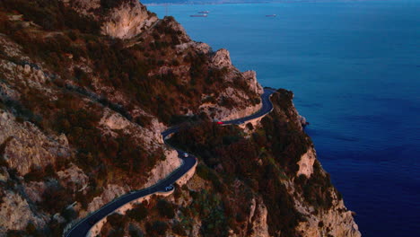 Largo-Y-Sinuoso-Camino-Alrededor-De-La-Costa-Roja-De-Amalfi-Al-Atardecer,-Sur-De-Italia-Con-Vistas-Al-Mar-Tirreno,-Vista-Aérea