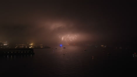 Independence-day-fireworks-exploding-over-misty-San-Francisco-bay,-California-aerial-view-across-marina-at-night