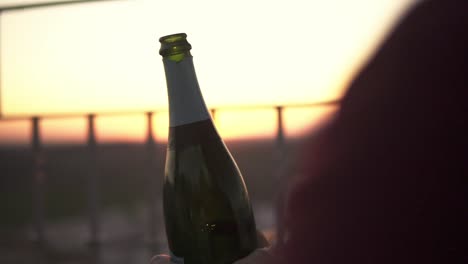 Slowmotion-shot-of-a-man-opening-a-bottle-of-prosecco-with-the-sun-setting