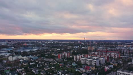 Riga-TV-tower-in-horizon-and-suburbs-cityscape,-aerial-view-with-orange-sky