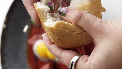 Woman's-Gentle-Hand-Dipping-Bite-Of-Bread-Into-Eggs-And-tomato-Sauce