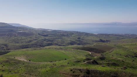 Aerial-view-of-rolling-landscape-with-Sea-of-Kinneret-in-background,-Israel