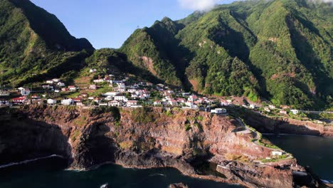 Aerial-view-of-a-town-on-a-volcanic-rocky-cliff-on-epic-green-Madeira-coast