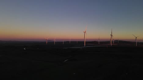 Drone-flying-towards-wind-turbines-on-wind-farm-at-dusk,-Valley-of-Tears,-Israel