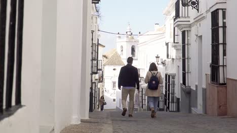 Slowmotion-shot-of-a-couple-walking-down-a-small-alleyway-with-small-white-apartments