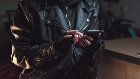 Hacker-wearing-mask-using-phone-dressed-in-leather-jacker-and-gloves