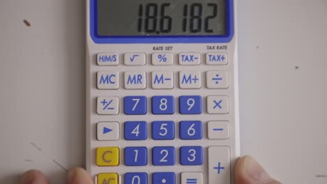 Finger-Drückt-Zahlen-Und-Multipliziert-Mit-Dem-Taschenrechner-Auf-Dem-Tisch