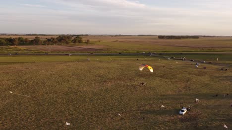 Motorized-paraglider-flying-at-low-altitude-over-rural-fields-at-sunset,-Argentina