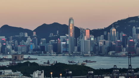 Aerial-wide-shot-showing-central-city-of-Hong-Kong-with-skyline-and-mountains-in-background-at-sunset