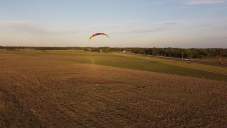 Motorized-paraglider-flying-over-rural-fields-at-sunset