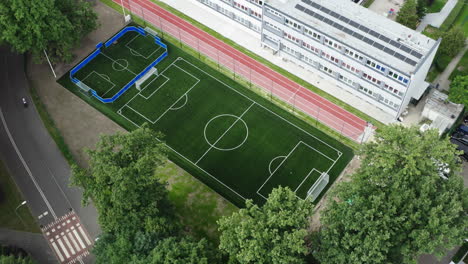 Flying-backwards-aerial-shot-of-a-brand-new-soccer-field-and-running-track-next-to-the-elementary-school-in-Poland,-4K-drone