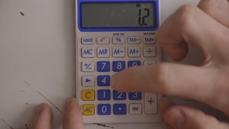Finger-Multiplying-Numbers-Using-A-Calculator.-closeup,-overhead