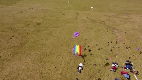 Aerial-top-down-shot-showing-colorful-flying-kites-during-windy-day-above-grass-field