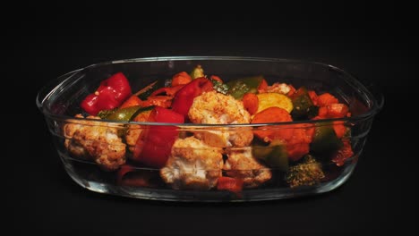 Medley-of-grilled-vegetables-in-a-glass-dish-against-black-background