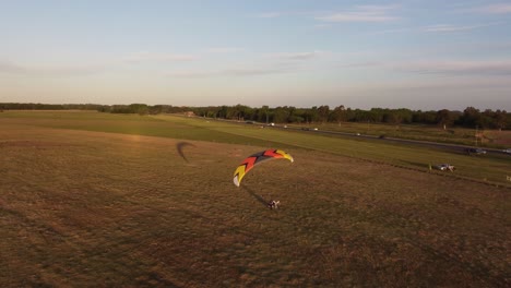 Aerial-tracking-shot-of-paratrike-paraglider-landing-on-grass-field-at-sunset---Traffic-on-road-in-background---Buenos-Aires,Argentina