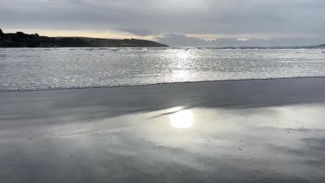 Slow-motion-wave-moving-on-a-sandy-beach-with-sun-glare-over-surface-in-wintertime