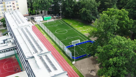 Flying-towards-a-brand-new-football-field-mad-with-artificial-grass-next-to-the-elementary-school-in-Poland,-4K-drone