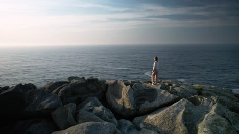 Weiblicher-Tourist,-Der-Auf-Felsen-Im-Sonnenlicht-An-Der-Küste-Von-Malpica-In-A-Coruña,-Spanien-Steht