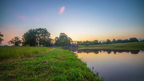 Green-riverbanks-at-sunrise-with-colorful-sky-reflecting-on-water-surface