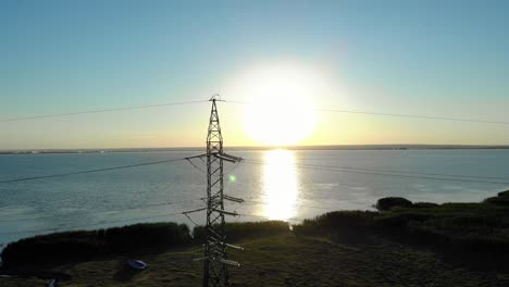 Transmission-Tower-With-Sun-Reflecting-In-The-Water-At-Sunrise-In-The-Background
