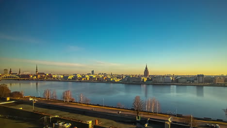 Todo-El-Día-Y-La-Noche-Lapso-De-Tiempo-De-La-Ciudad-De-Riga,-Letonia-Desde-El-Otro-Lado-Del-Río-Daugava