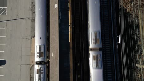 A-top-down-view-directly-over-a-train-station-platform-as-two-trains-arrive-on-a-sunny-day