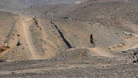 Single-mountain-biker-going-down-a-hill-picking-up-speed-and-jumping-over-the-hill-and-riding-away-safely