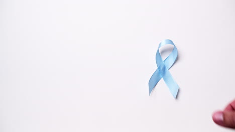Detail-of-male-hand-placing-ribbon-in-light-blue-color-on-white-background