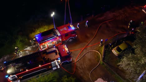 Ein-Gewirr-Von-Feuerwehrautos-Und-Feuerwehrschläuchen,-Die-Nachts-Auf-Einer-Unbefestigten-Straße-Von-Oben-Gesehen-Werden