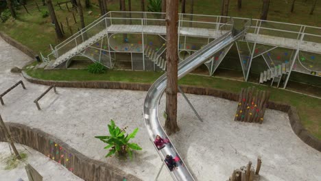 Aerial-tracking-two-kids-playing-on-children's-curved-slide-with-the-ground-lots-of-white-sand