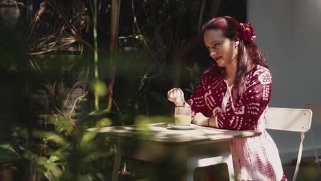Establishing-dolly-shot-of-an-attractive-Caucasian-Female-sitting-at-an-outdoor-garden-table,-slowly-stirring-her-morning-coffee-in-the-sun