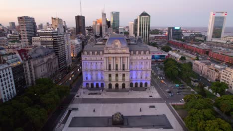 Dolly-in-aerial-view-of-the-front-of-the-Kirchner-Cultural-Center-illuminated-with-blue-lights,-city-at-night-during-the-blue-hour,-Buenos-Aires,-Argentina