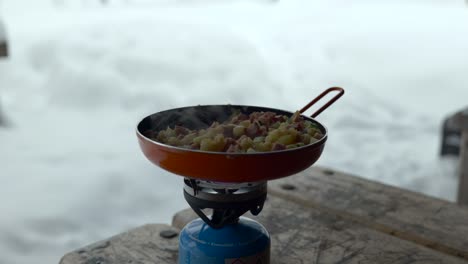Cooking-food-in-a-orange-pan-outdoors-in-a-snowy-landscape