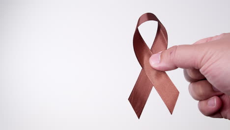 Detail-of-male-hand-holding-ribbon-in-brown-color-over-white-background