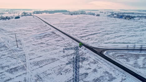 Engineer-repairing-cables-atop-a-tall,-metal-lattice-transmission-tower---aerial-view