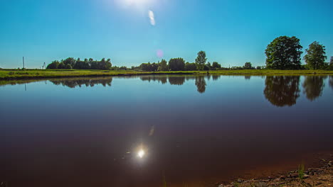 Amazing-timelapse-of-a-lake-with-ripples-In-the-water-and-the-sun-setting-behind-lush-green-trees-on-a-idyllic-summer-day