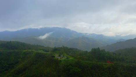 A-drone-flies-forward-through-the-mist-to-reveal-a-lush,-tropical-valley-nestled-between-mountains,-with-a-rainy-atmosphere-enhancing-the-serene-beauty-of-the-landscape