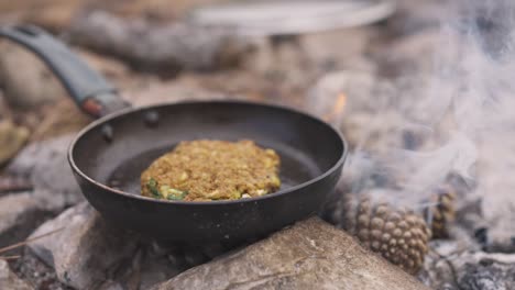 Vegan-lentil-burger-on-pan,-cooking-food-using-bonfire,-outdoor-camping