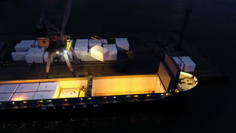 Crane-loading-the-hull-of-a-cargo-ferry-at-nighttime---aerial-orbit