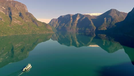 Aerial-tilt-up-giant-Cruiser-on-Green-Tranquil-Fjord-Water-between-Mountains-in-Norway