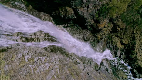 Aufsteigender-Schuss-Von-Oben-Nach-Unten-Eines-Kaskadierenden-Wasserfalls,-Der-Felsige-Berge-Hinunterstürzt