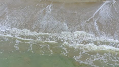 Die-Kamera-Fängt-Die-Schönheit-Eines-Tropischen-Strandes-Von-Oben-Ein-Und-Bewegt-Sich-Langsam-Nach-Unten,-Um-Den-Markanten-Kontrast-Des-Weißen-Schaums-Und-Des-Türkisfarbenen-Wassers-Zu-Zeigen,-Während-Die-Wellen-Auf-Das-Sandige-Ufer-Schlagen
