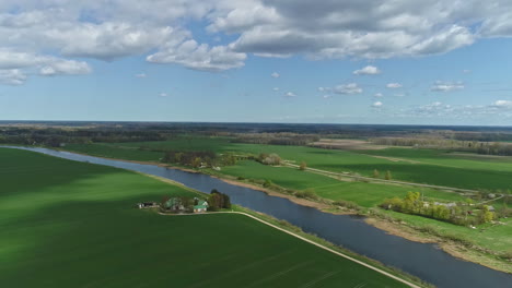 Aerial-drone-video-shot-of-wide-green-grass-field-and-long-river-in-a-village
