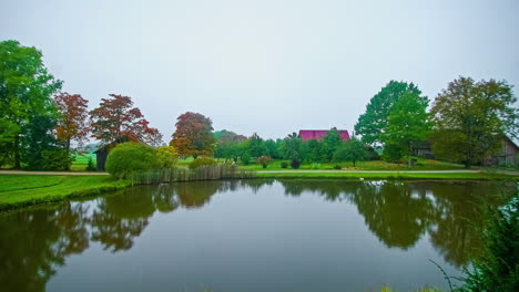 Lake-in-bucolic-and-idyllic-verdant-landscape-with-red-roof-in-background