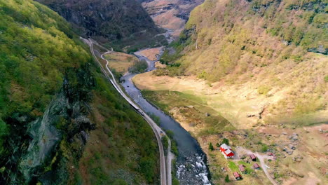 A-river-flowing-through-a-steep-valley-with-a-train-on-the-railroad-tracks---aerial-view