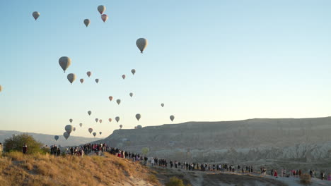 Heißluftballons-Fliegen-über-Menschen-Auf-Einem-Hügel-über-Kappadokien,-Türkei,-Zeitlupe